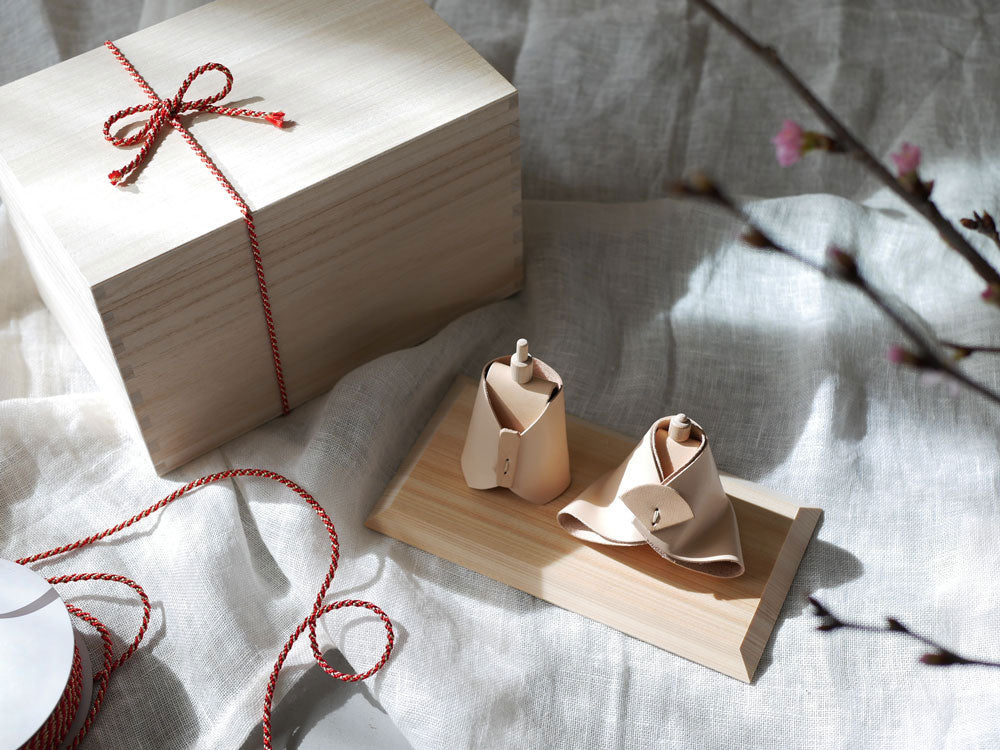 Comore Sunブランドのヌメ革製お雛様。伝統的な着物をまとい、ヒノキの頭部と台座を持つ小型で手作りの美しいお雛様です。