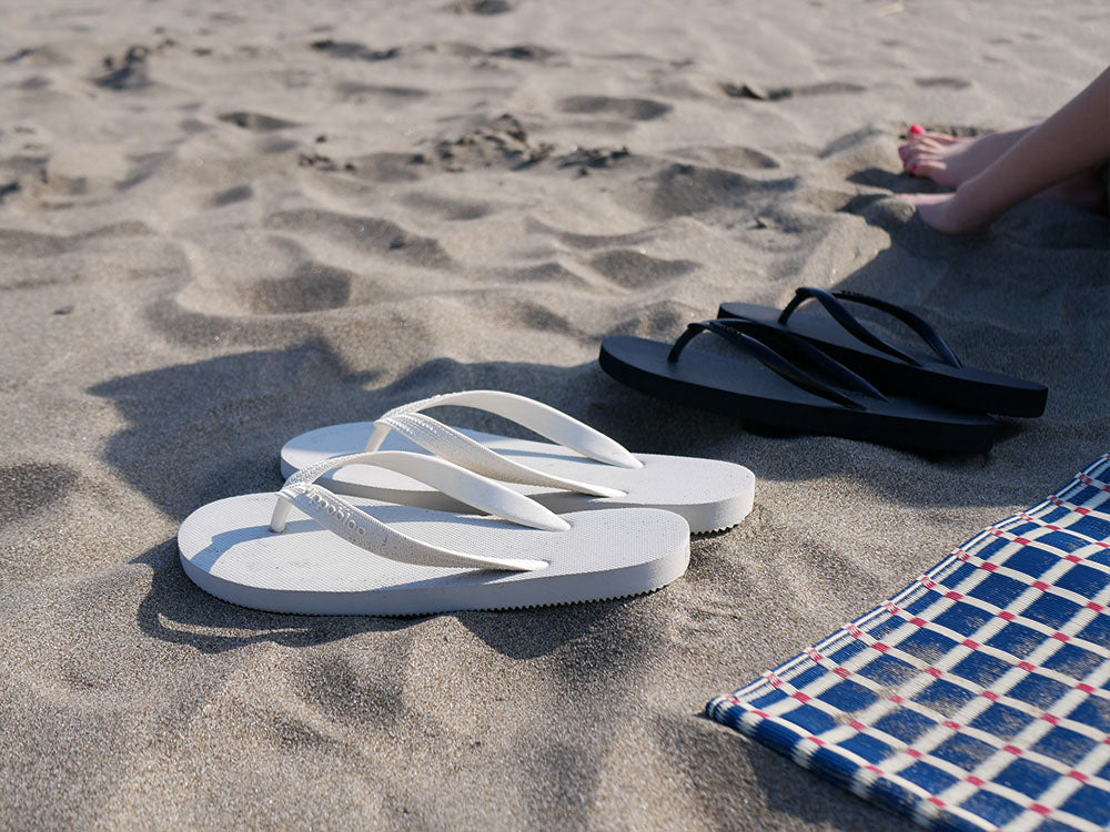 砂浜にグレーのビーチサンダルと足の影が映る様子