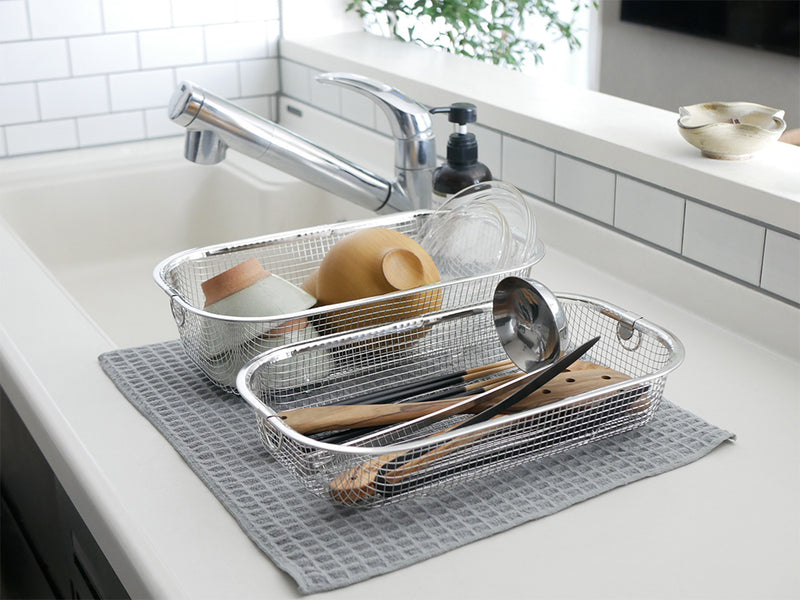 キッチンシンクに置かれたステンレス製のすっきり暮らす水切りかご。テーブルウェアや調理器具が整然と収納されています。