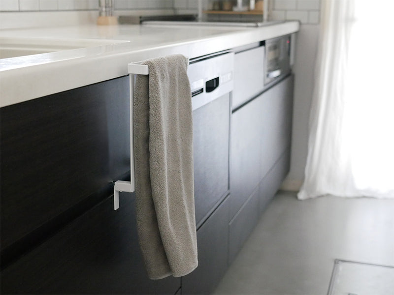 グレーの床とシルバーの配管設備が調和するキッチンシンク下に設置されたタワータオルハンガーのモダンな収納スペース