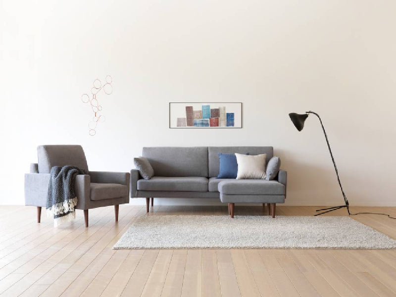 高野木工のLEOカウチソファが木製フローリングのリビングルームに配置され、アームレスト付きチェアとスタイリッシュなランプがアクセントとなっている様子