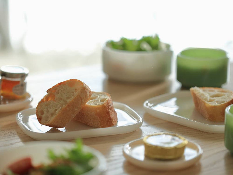 ideacoのミルクガラス製スクエアプレート2個セットが食卓に並べられ、パンや食器と共に配置されている様子