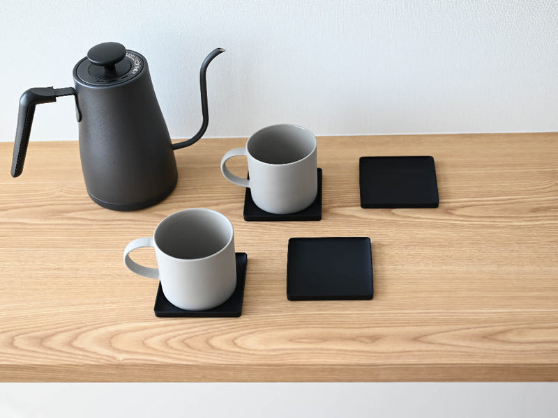 シリコーン製の【tower/タワー】立体コースターがカップやティーポット、電子機器と共にテーブル上に並べられています