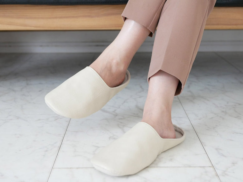 サラサデザインの白色ルームシューズ。合成皮革を使用したファッション性の高いくるぶし丈スリッパ。快適な履き心地を提供します。