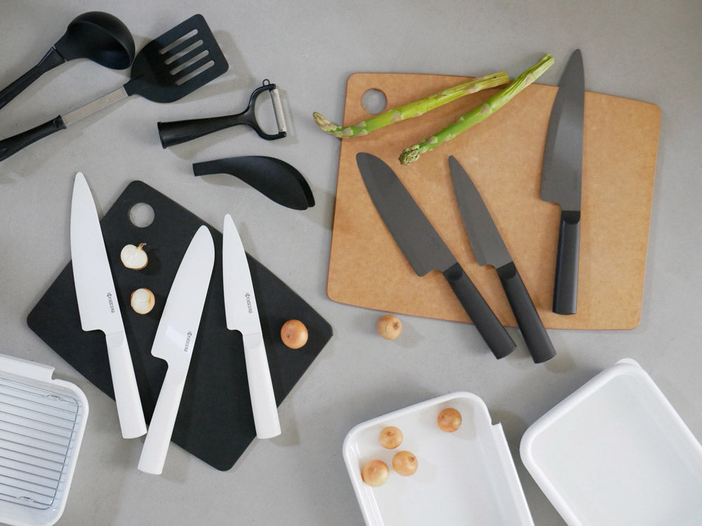 京セラ製セラミック包丁が木製まな板の上に美しく配置され、新鮮な野菜や果物と共に写っています