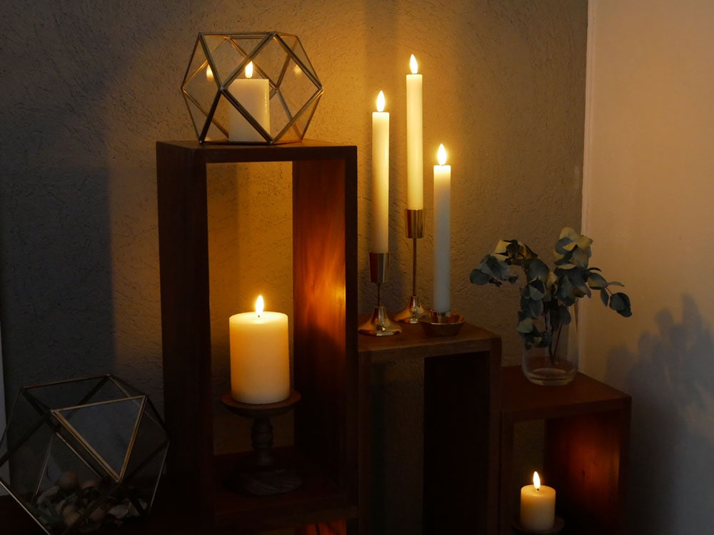 真鍮フレームのガラスケースにフィギュアが飾られ、周囲に炎付きキャンドルが配置された静物写真