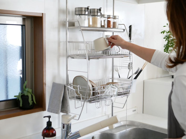 キッチンカウンターに設置されたステンレス製の【bws SELECTION】流れるつっぱり水切りラックで、食器や調理器具が乾かされています