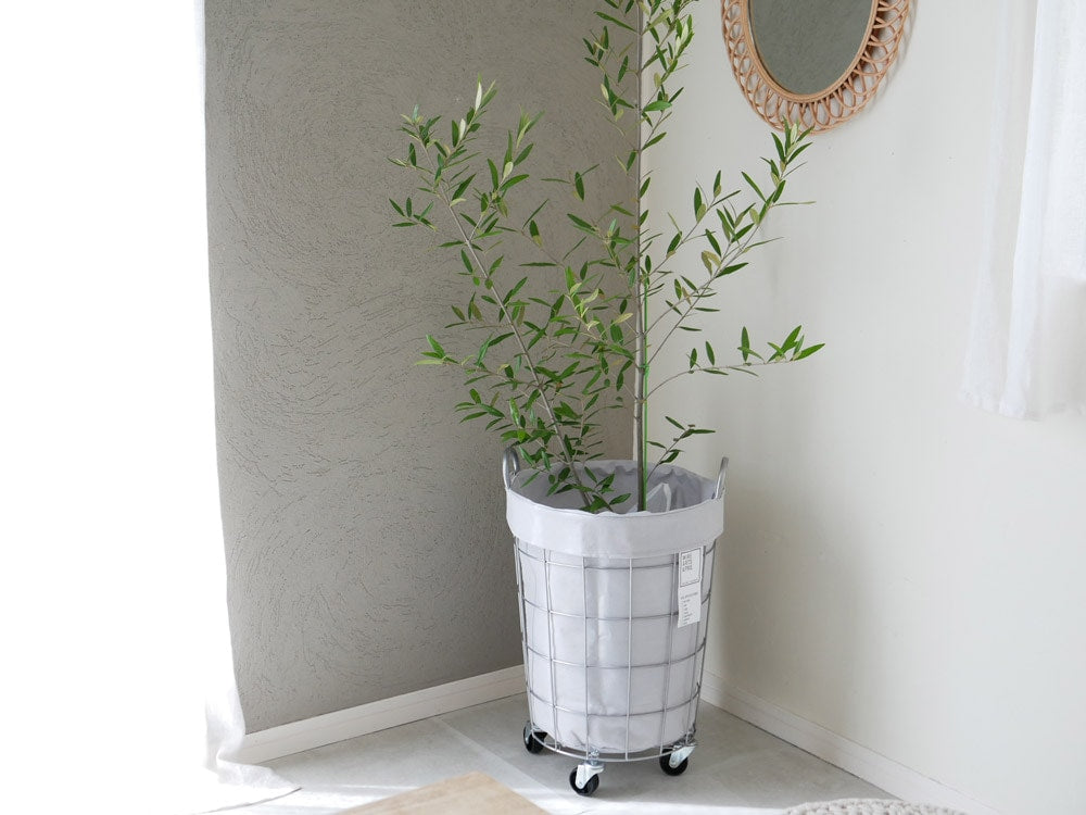 BRIDのスチール製ランドリーストレージ ラウンド33Lが木製の椅子と花瓶、植物と共にインテリアとして配置されている様子