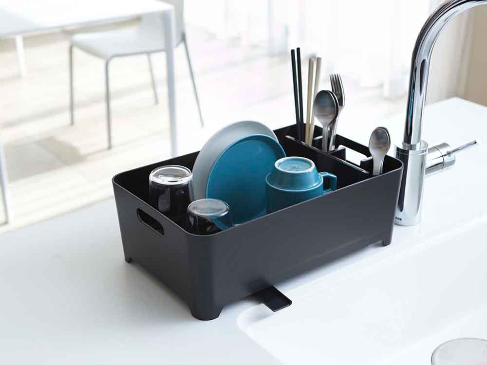 キッチンシンクに置かれたYAMAZAKI/towerの水切りバスケットとプラスチック製のキッチン用品、鉢植え植物が配置されている様子