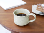 南窯/EDITIONSの荒粉引手作りマグカップが木製のテーブル上に置かれている