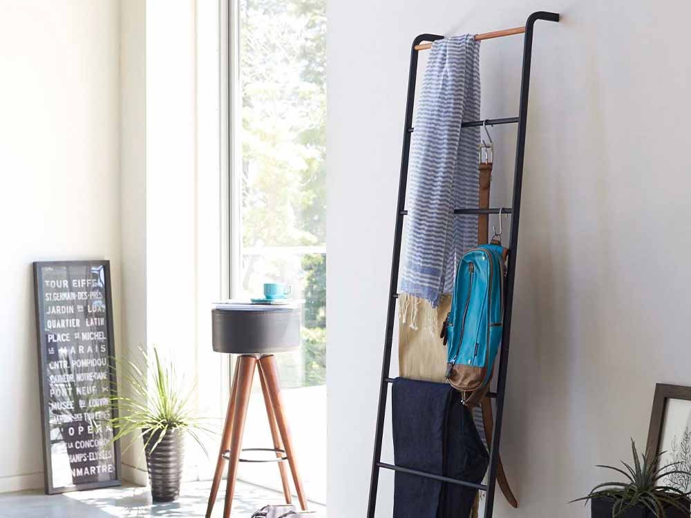 Yamazaki/towerのタワーラダーハンガーが木製の棚に設置され、観葉植物とバスケットが配置されている室内の写真