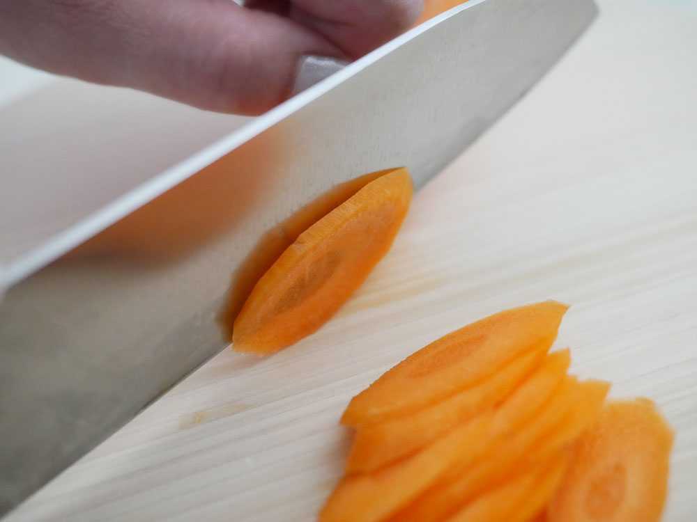 ヒノキの立つまるいまな板に包丁と野菜が置かれている