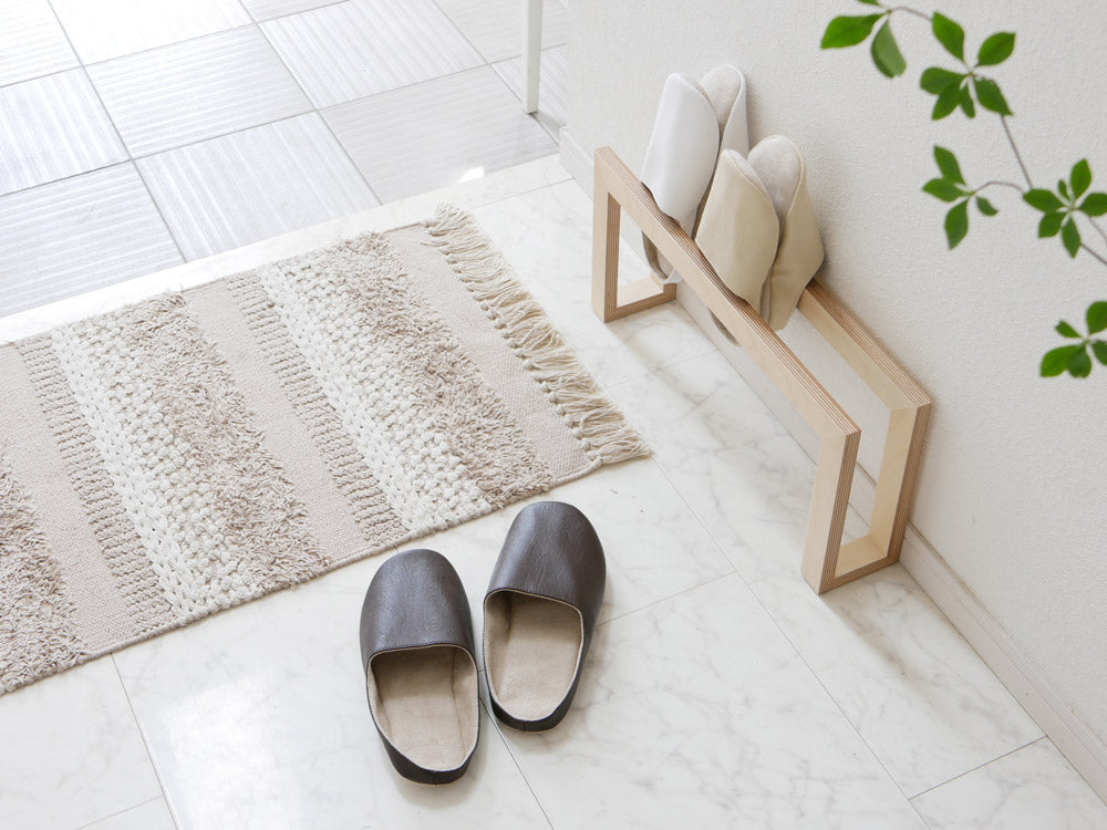 サラサデザインのグレーのプレーンステッチルームシューズがリビングルームのカーペット上に置かれている