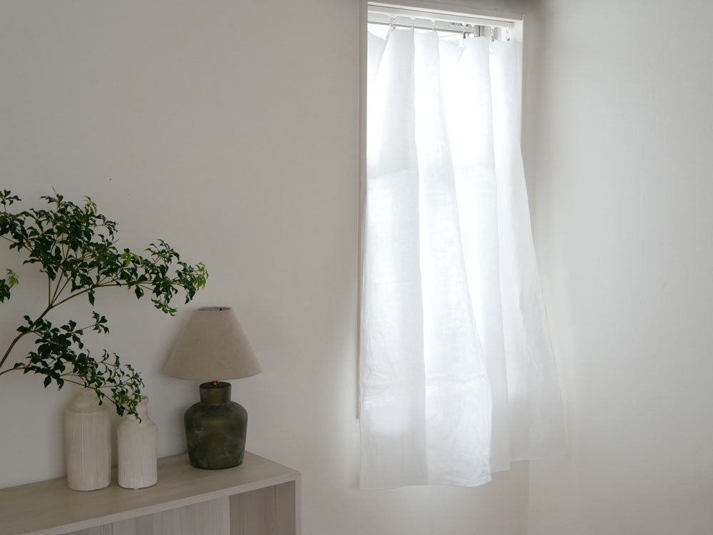 リネン100%素材のクリップ留めカーテンが窓に掛けられており、ナチュラルな風合いとシンプルなデザインが特徴的な室内の様子