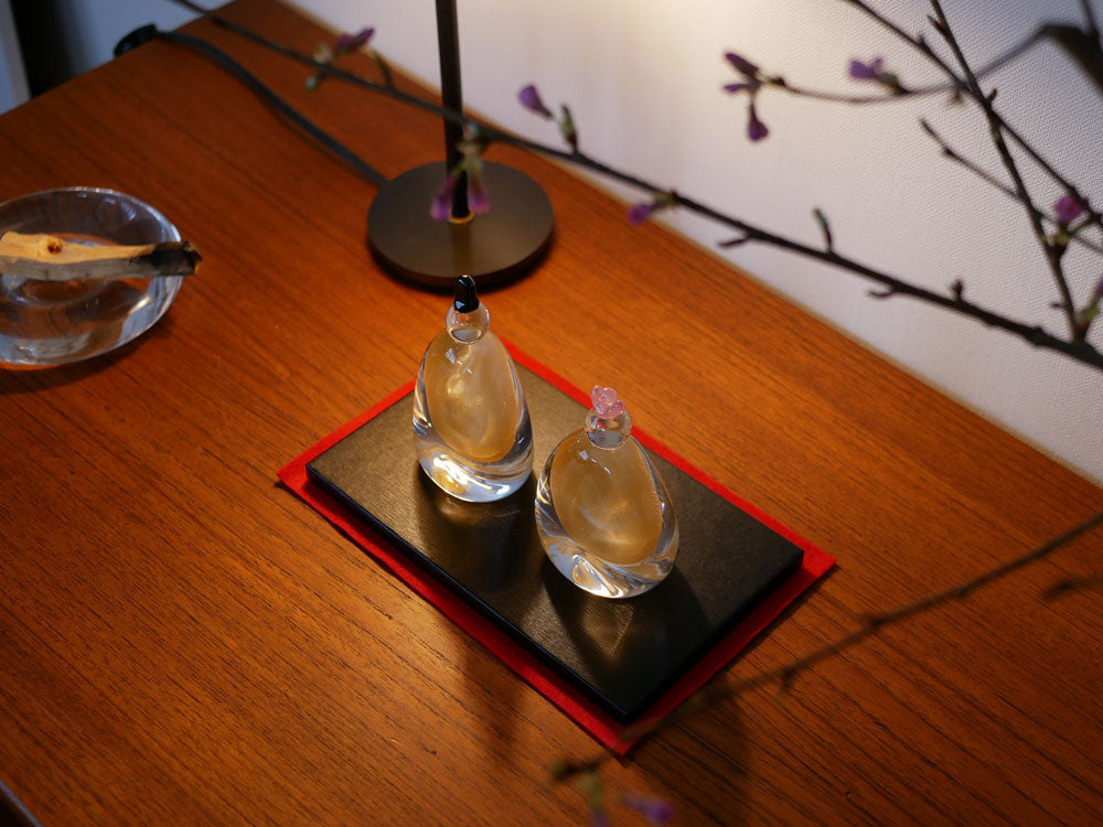 硝子屋PRATO PINOの手作りガラス製お雛様セット。お内裏さまとお雛さまが木箱と飾り台に並んで展示されています。