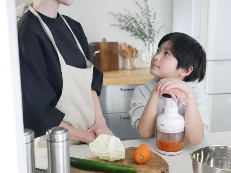 キッチンカウンター上でOXOチョッパーを使い、食材を刻む大人の手とそばにいる子供の様子