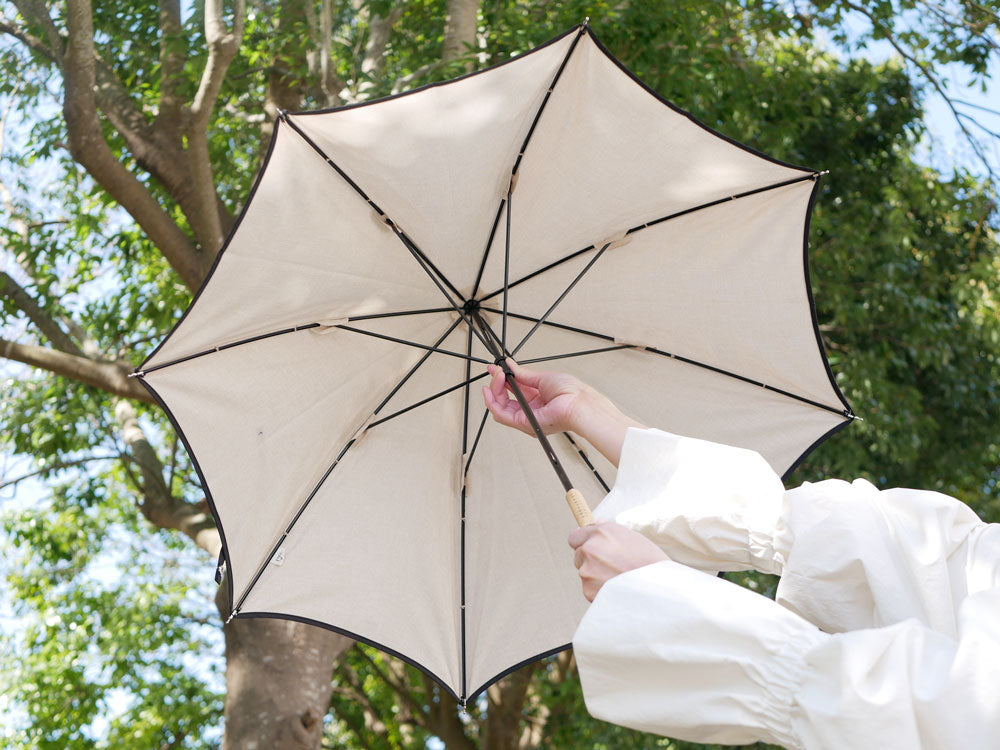 because（ビコーズ）のプレーンパイピング傘。防水加工のポリエステル生地とラタン＋レザーのハンドルを備えた晴雨兼用タイプ。