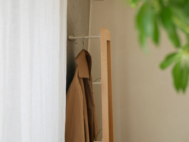 天然木フレームのリヴ立て掛けミラーと衣類ハンガー、タオルが配置された室内の様子