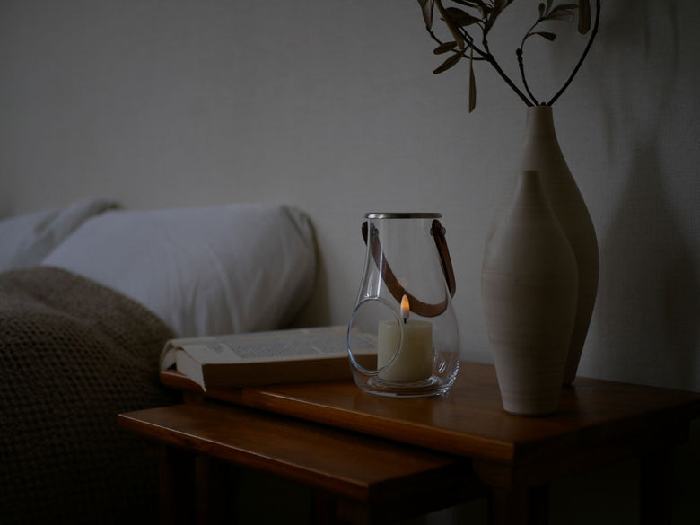 無鉛ガラスと皮革製のホルムガードランタンが木製テーブル上に配置され、柔らかな光を放つ静物写真