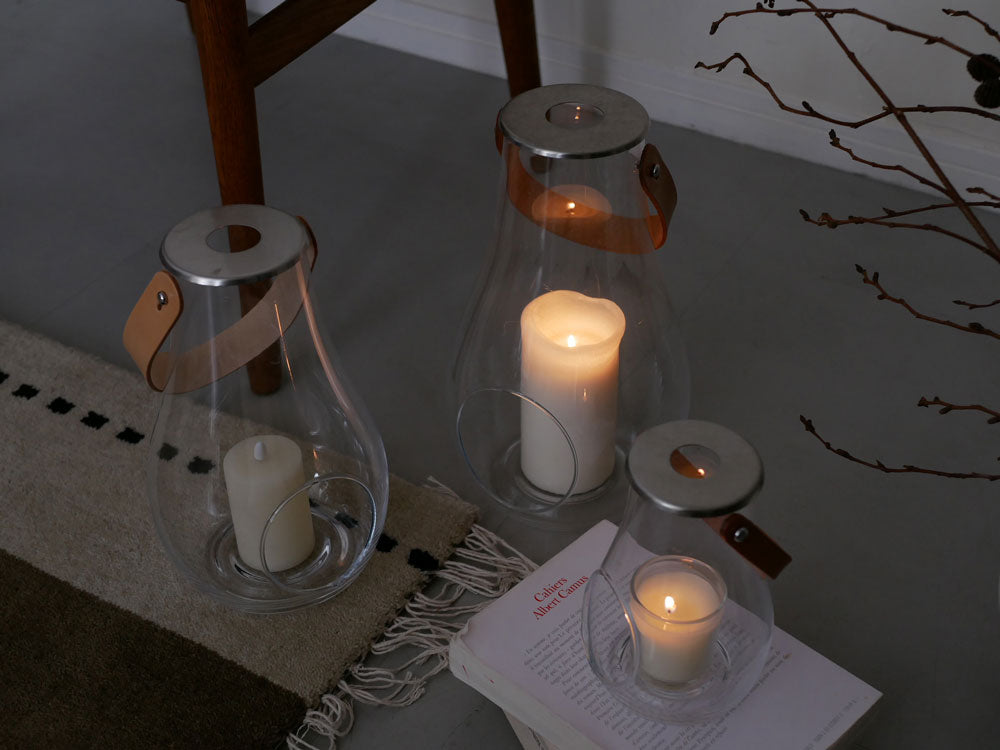 ホルムガードのDESIGN WITH LIGHTランタン。無鉛ガラスとステンレススチールを使用し、キャンドルとともに美しく照らされた透明なランタンの静物画像。