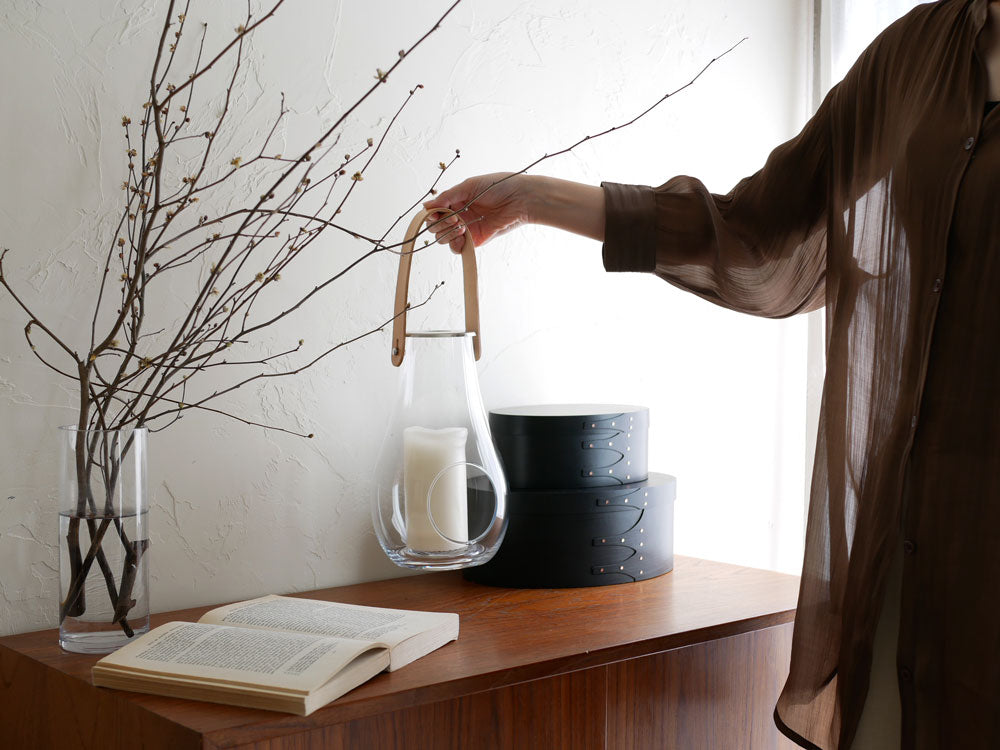 ポーランド製HOLMEGAARD DESIGN WITH LIGHTランタンと陶器の花瓶に飾られた観葉植物、ステンレス鋼の照明が調和したインテリアセット