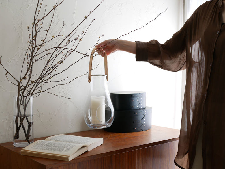 ポーランド製HOLMEGAARD DESIGN WITH LIGHTランタンと陶器の花瓶に飾られた観葉植物、ステンレス鋼の照明が調和したインテリアセット