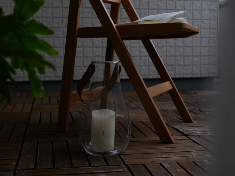 ホルムガード DESIGN WITH LIGHT ランタンが木製の床と家具、ガラス製の花鉢とともに配置されたスタイリッシュな静物写真