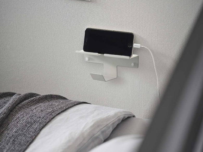 銀色のスチール製ウォールスマートフォン＆ヘッドホンホルダーが壁に取り付けられている様子。テクノロジー感のあるモダンなデザイン。