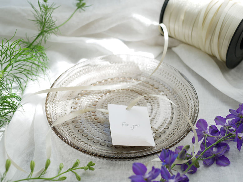 フィンランド製イッタラカステヘルミプレートがテーブルクロスの上に置かれ、銀のカトラリーやキッチン用品と共に整えられているダイニングセットの様子