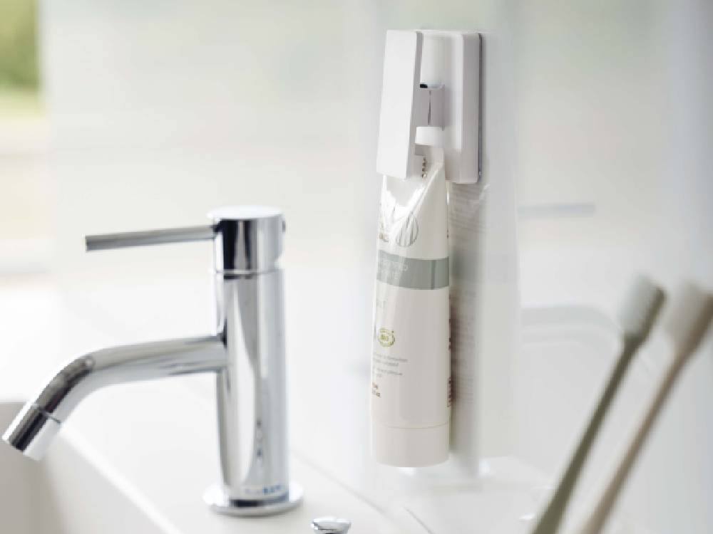 白い壁に取り付けられた【MIST/ミスト】フィルムフック ワイドクリップ2個組が、ボトルやソープディスペンサーなどのパーソナルケア用品を整理している様子