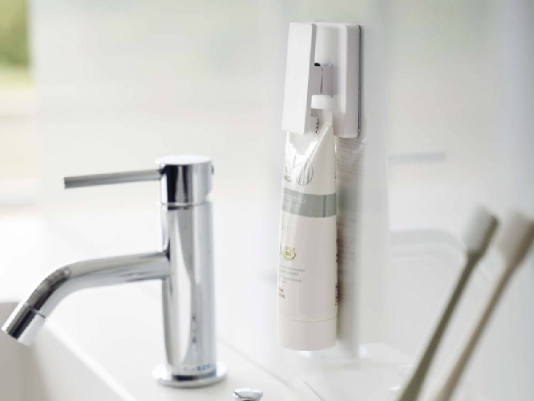 白い壁に取り付けられた【MIST/ミスト】フィルムフック ワイドクリップ2個組が、ボトルやソープディスペンサーなどのパーソナルケア用品を整理している様子