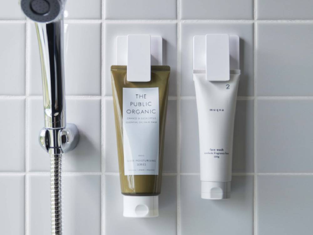 ワイドクリップ付きフィルムフックがバスルームの光沢ある壁面に取り付けられ、化粧品ボトルやヘアケア用品を掛けている様子