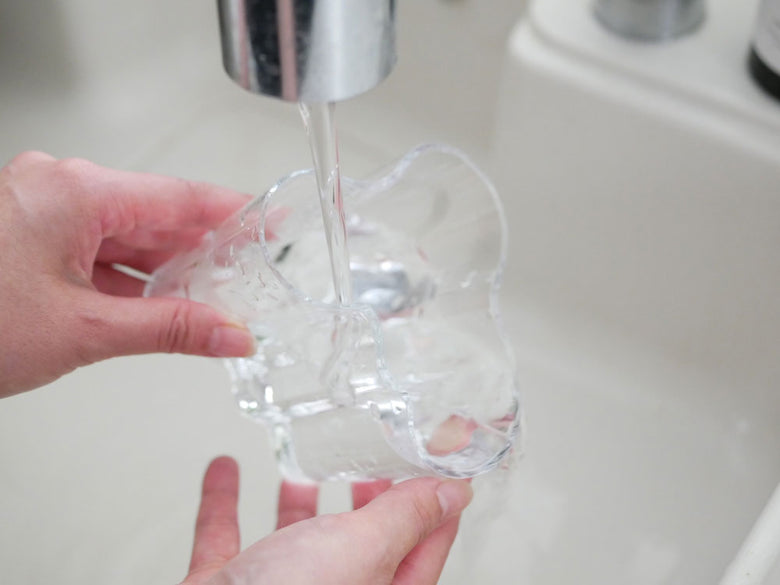 フィンランド製イッタラ・アルヴァ・アアルトコレクションの無鉛ガラスグラスに水と氷が入っており、シンクの蛇口の上に置かれている様子