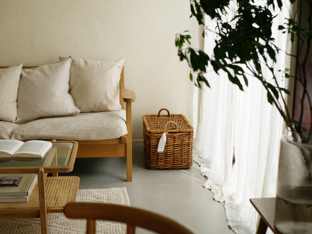 Creer/クレエのラタン製運べる収納バスケットがリビングルームに配置され、クッションや観葉植物と調和したナチュラルなインテリアを演出しています