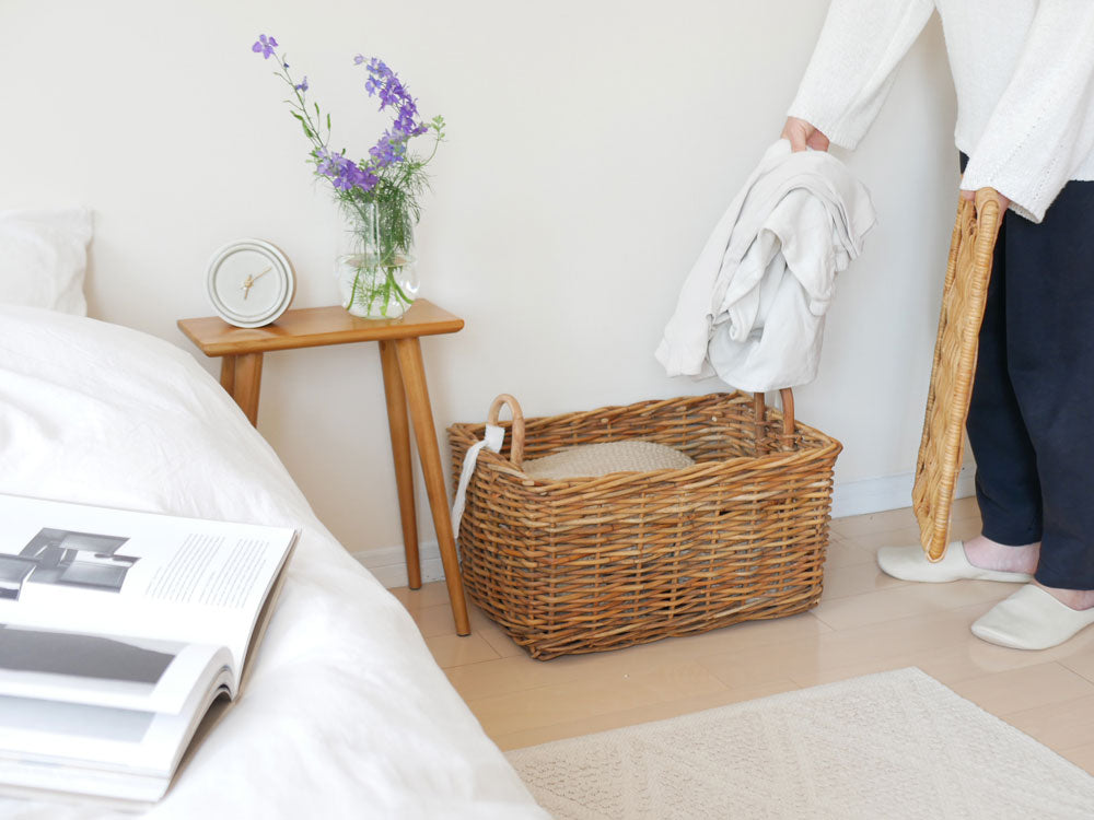 インドネシア製の皮つきラタンで作られた運べる収納バスケットが木製家具の上に置かれ、花瓶や鉢植え植物とともに自然素材のインテリアとして配置されている様子