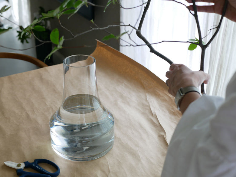 BOB CRAFT製ソーダガラスの透明な花瓶が机の上に置かれ、室内植物やランプとともに飾られています。