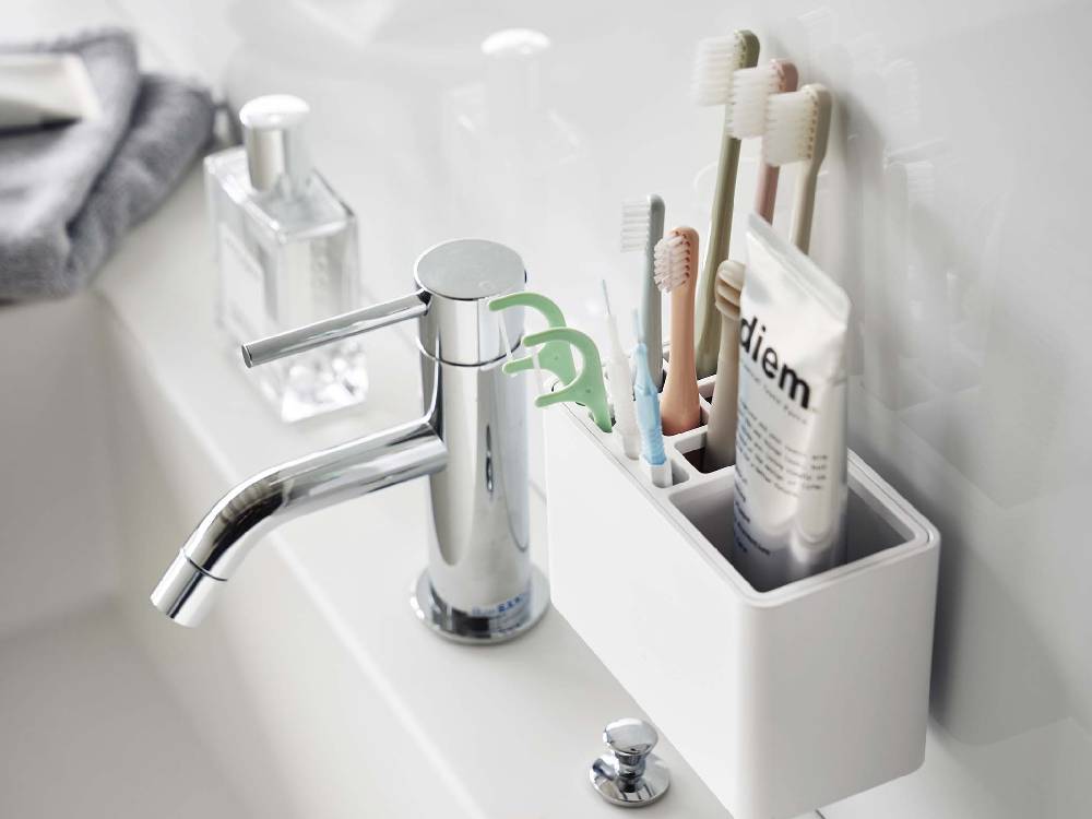 浴室のシンク横に設置された【MIST/ミスト】フィルムフック歯ブラシスタンド。シンプルなデザインで、歯ブラシやソープディスペンサーを整理し、緑の観葉植物がアクセントになっています。
