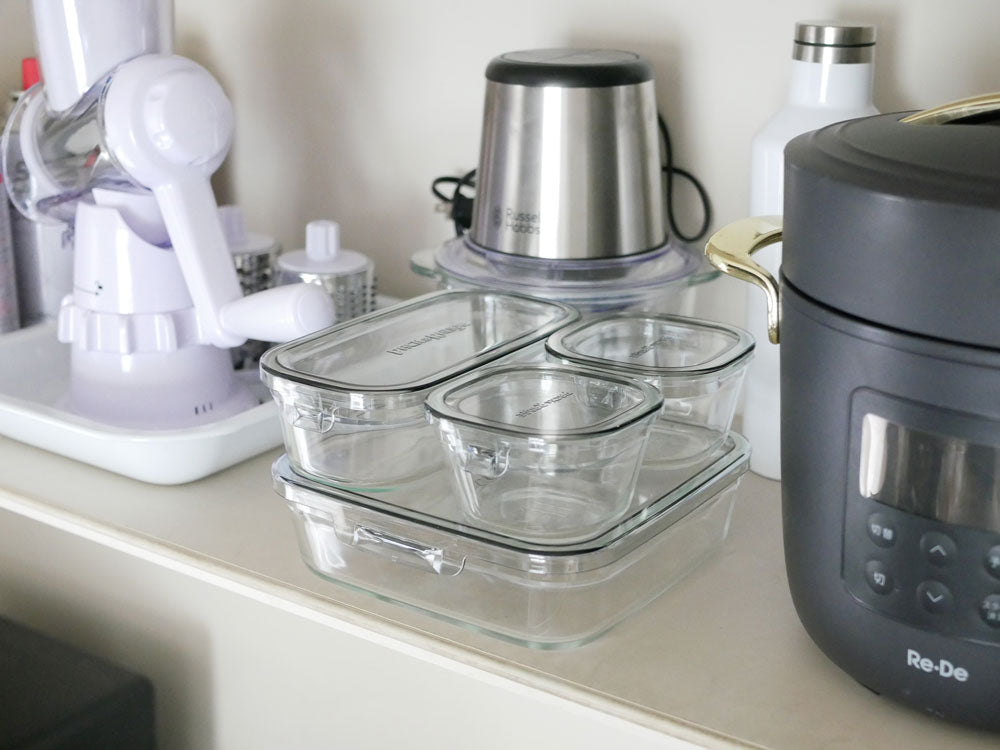 イワキのパック&レンジ システムセットの異なるサイズの耐熱ガラス容器とポリカーボネート製フタがキッチンのカウンタートップに並んでいる写真