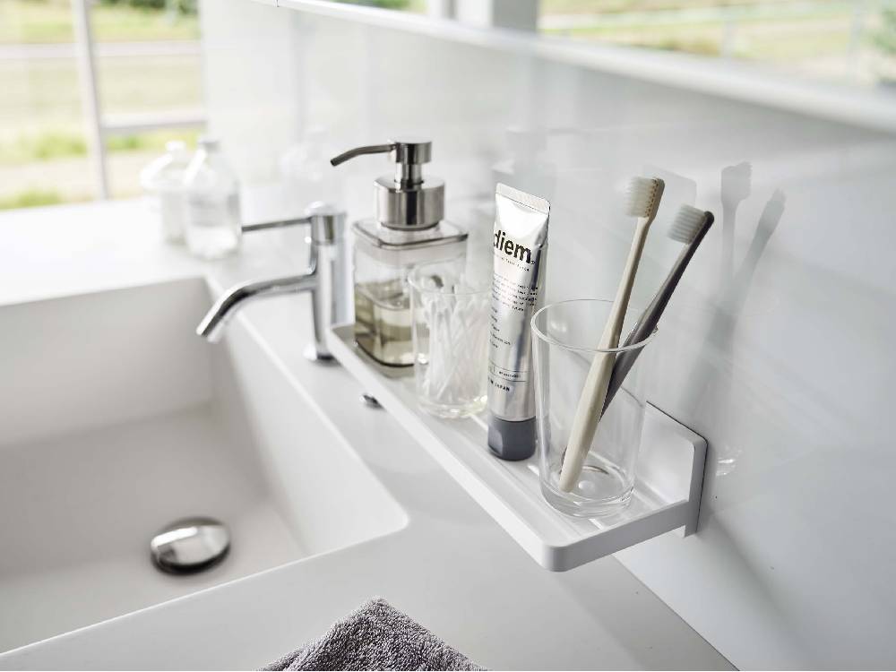 浴室の洗面カウンターに取り付けられた【MIST/ミスト】フィルムフック トレー W30。蛇口やボトルなどのパーソナルケア用品を整理整頓しています。