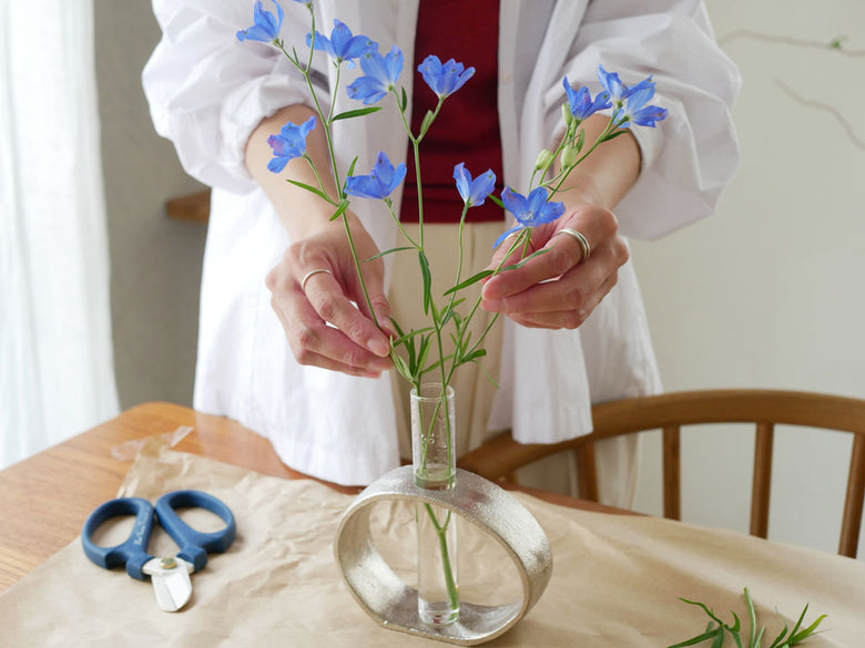 青い人工花がアルミガラスベースの花瓶に美しくアレンジされた花束の画像