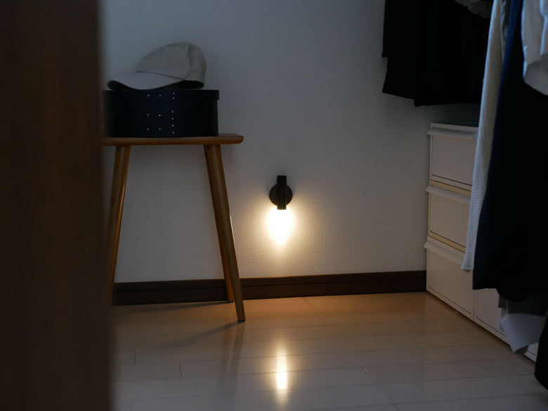 木製とアクリル樹脂で作られたスティック型センサーライトが木床の上に置かれ、暖色系のLED光を発している室内照明