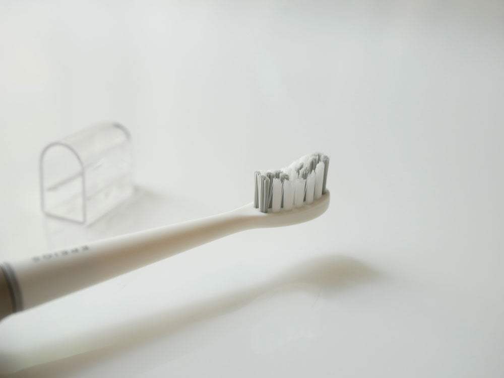 EPEIOSの音波電動歯ブラシ本体、替えブラシヘッド2本、携帯用ケースがプラスチック製の背景に並べて配置されている