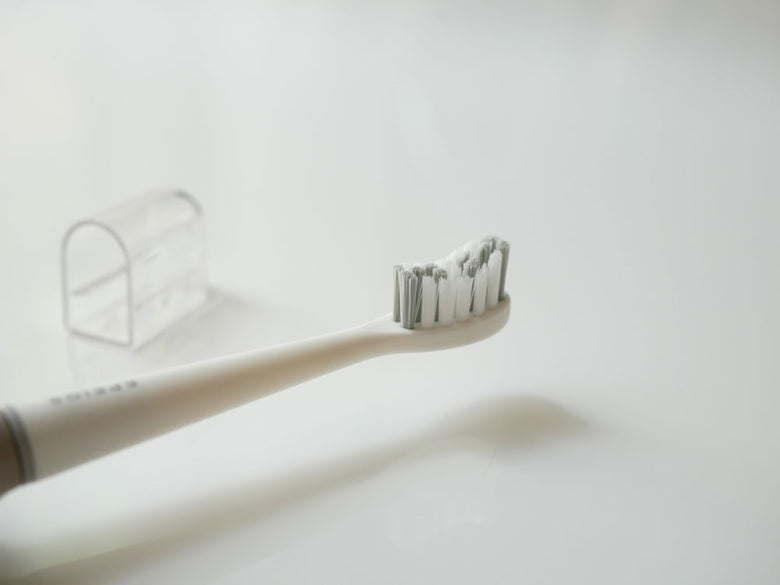 EPEIOSの音波電動歯ブラシ本体、替えブラシヘッド2本、携帯用ケースがプラスチック製の背景に並べて配置されている