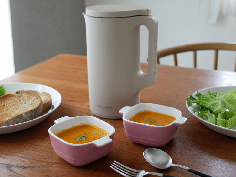 クリームホワイトのrecolte自動調理ポット本体とフタ、計量スプーン、お手入れブラシがセットになったキッチン家電