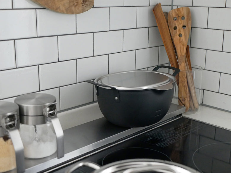 aikata（アイカタ）の楕円形コンパクト鉄製揚げ鍋と18-8ステンレス製の蓋および揚げザルがキッチンのカウンター上に配置されている様子