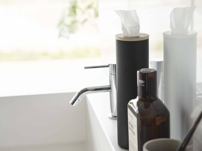 洗面台の上にスチールと天然木で作られた【RIN/リン】ボトル型ティッシュケース Sが置かれ、ソープディスペンサーやペーパータオルブラシなどのバス用品と共に整然と配置されている様子