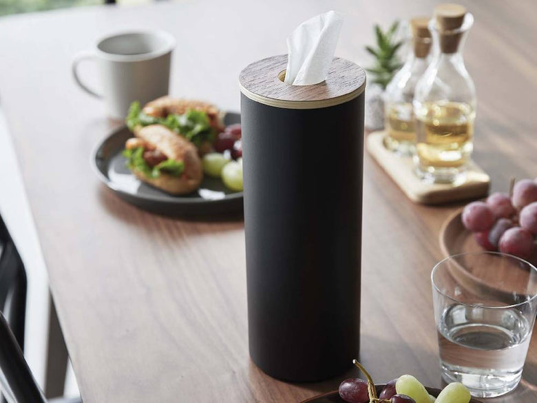 スチールと木材で作られたボトル型ティッシュケース Lが、カップやスプーン、ストローなどの食器と共にテーブルに配置されている