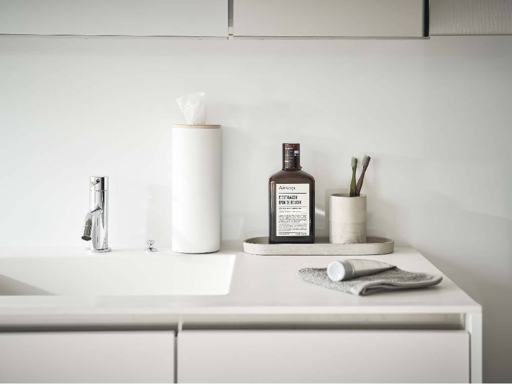 スチールと天然木のボトル型ティッシュケースがセラミックシンクと銀色の蛇口が配置されたカウンタートップに置かれたバスルームインテリア