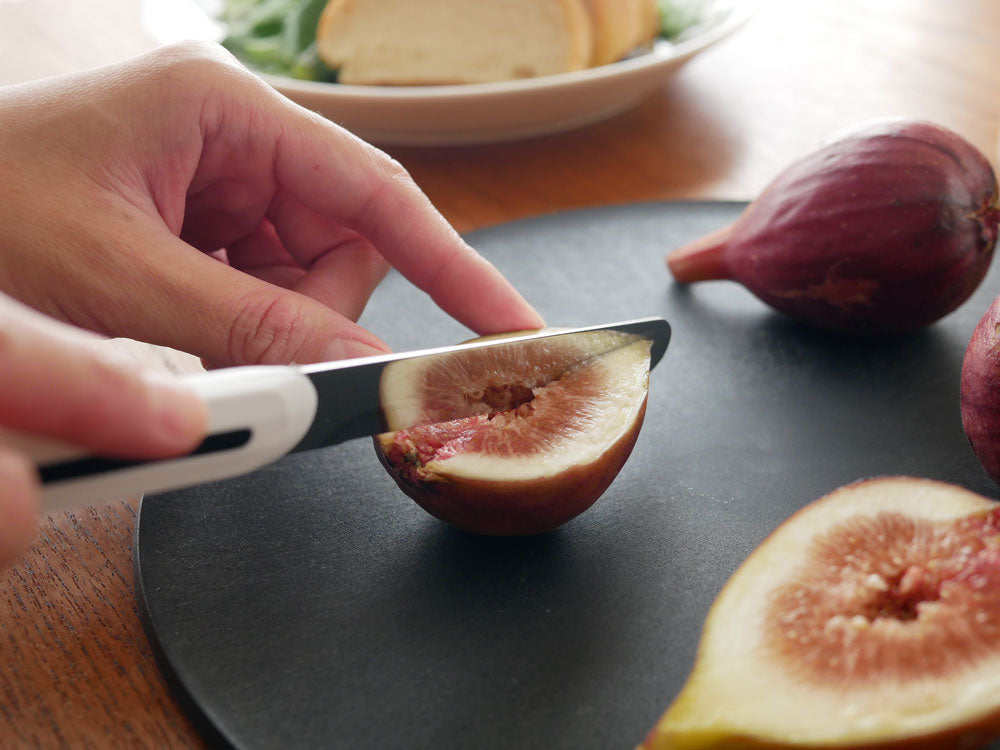 スペイン製ARCOSのパールホワイトおよびブラックテーブルナイフが木製カッティングボードと新鮮な果物と共に食卓に整然と並べられている様子