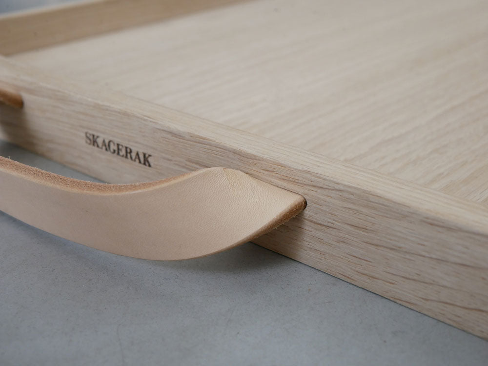 オーク材とレザーで作られたFRITZ HANSENのSkagerak Norr Trayが、キッチン用具やカッティングボードと共にテーブル上に美しく配置されている様子